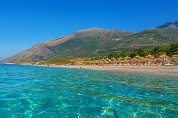 Vue sur l'eau turquoise et une plage en Albanie avec la montagne derrière